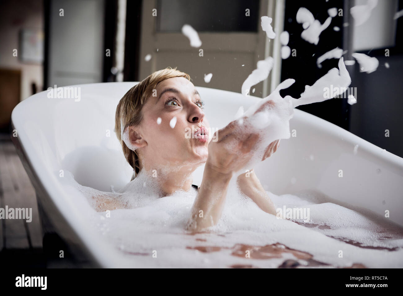 Blond woman taking bubble bath blowing foam in the air Stock Photo