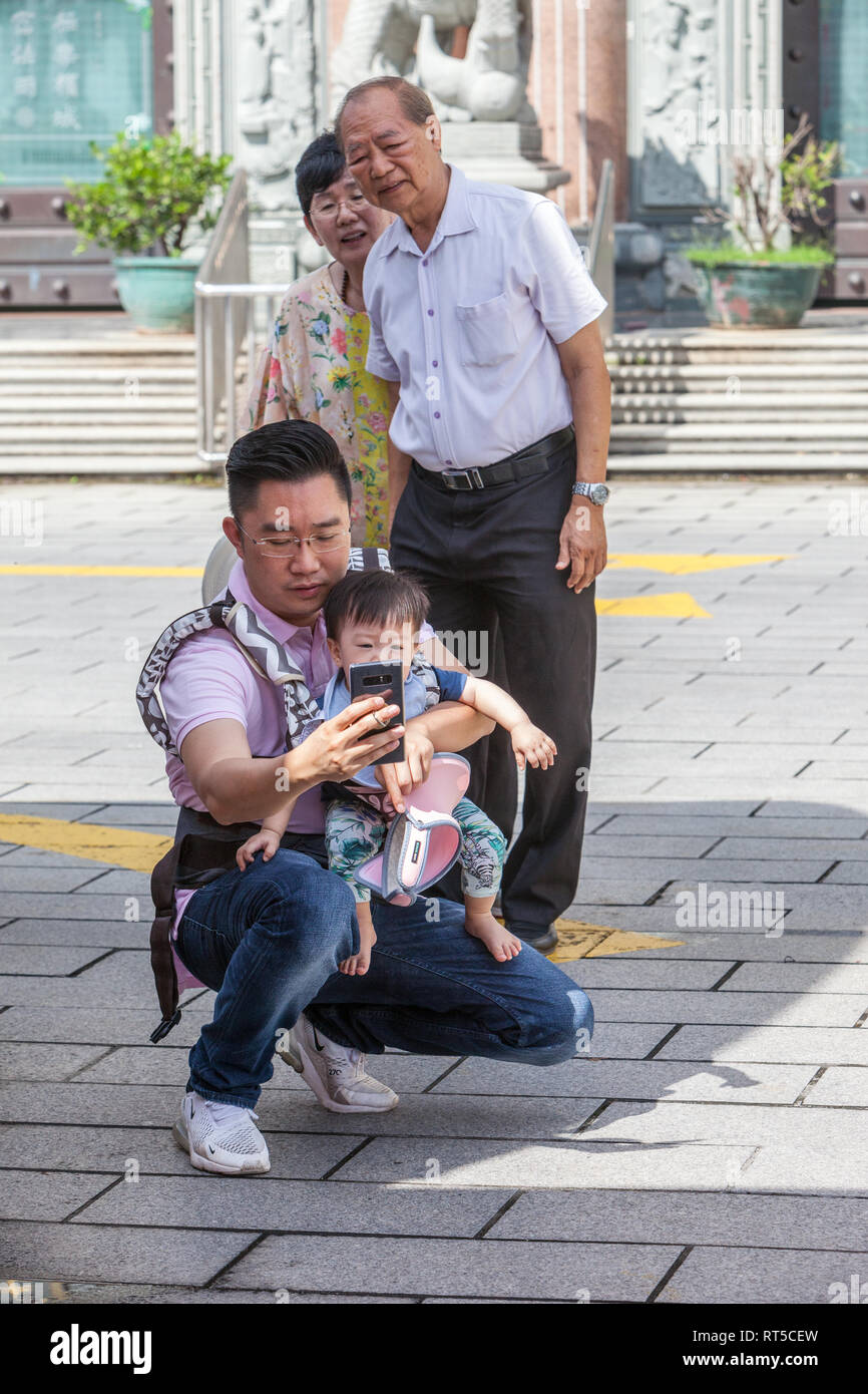 Grandparents Watching Father Take a Selfie at Kek Lok Si Buddhist Temple, George Town, Penang, Malaysia. Stock Photo