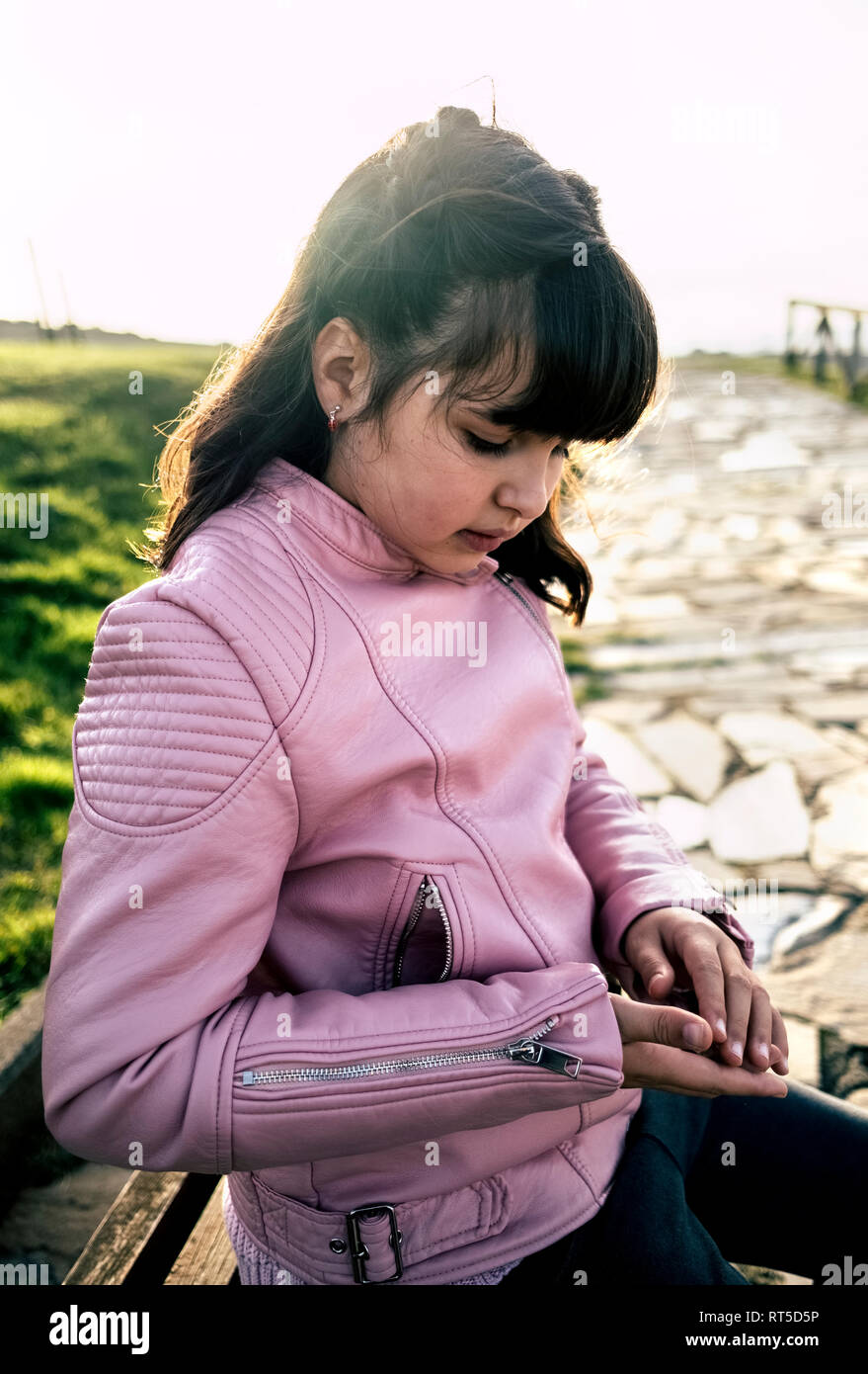 Girl wearing pink leather jacket looking at pebble in her hand Stock Photo