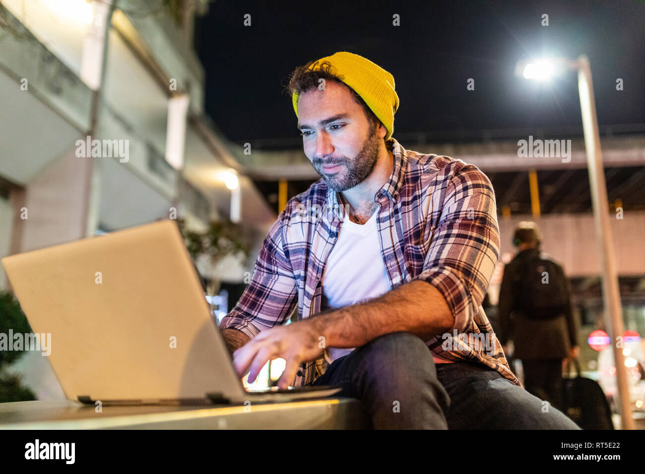 UK, London, smiling man using laptop out in the city at night Stock Photo