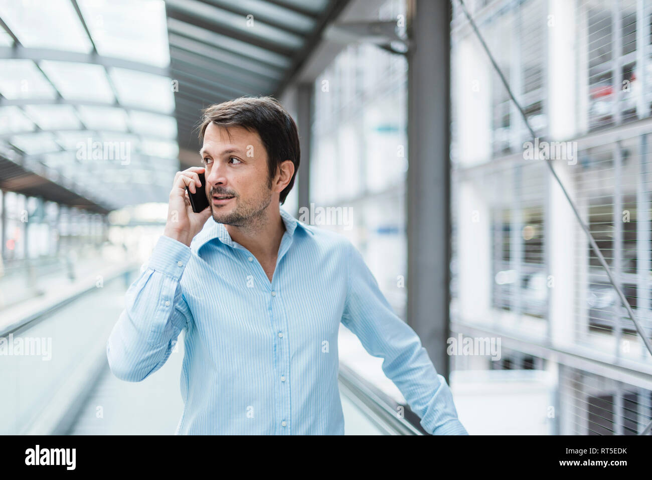 Businessman on a moving walkway, using smartphone Stock Photo