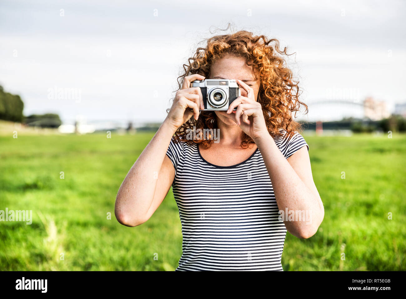 Young woman on a meadow taking picture of viewer with camera Stock Photo