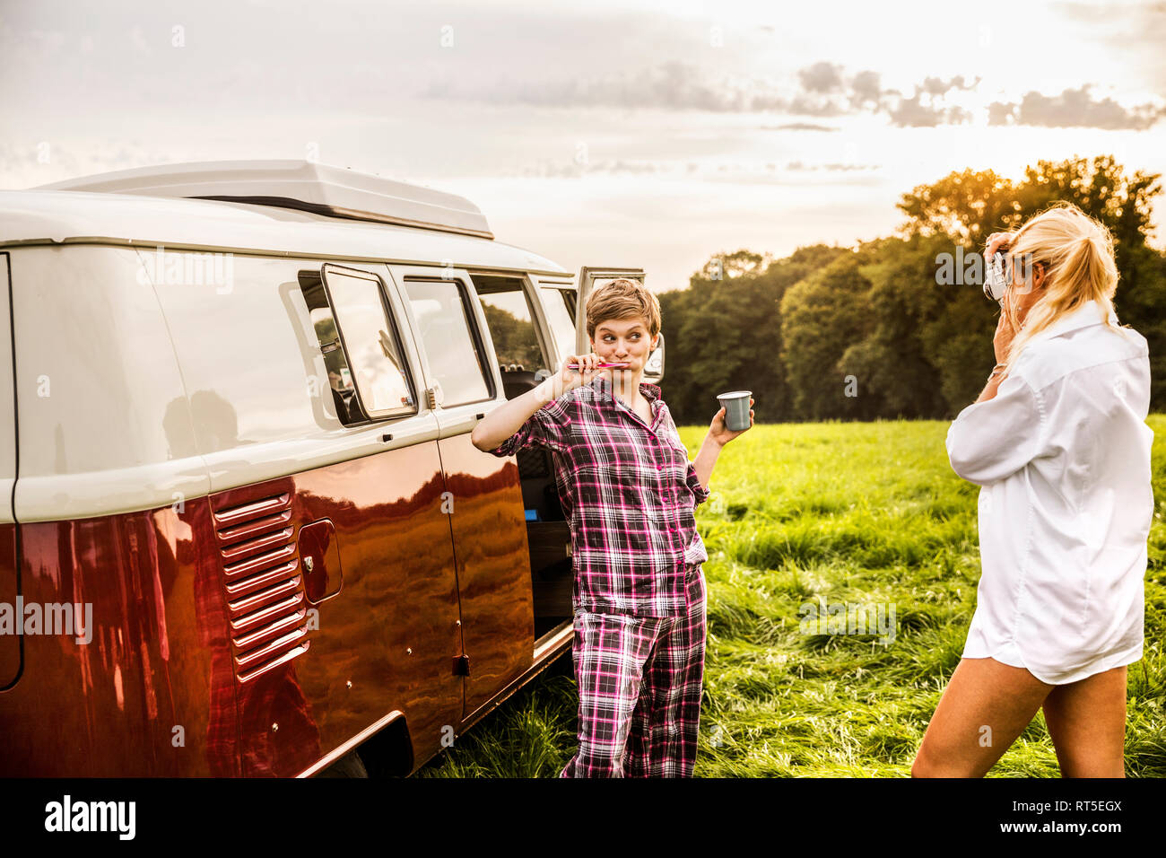 Woman taking picture of friend brushing teeth at a van in rural landscape Stock Photo