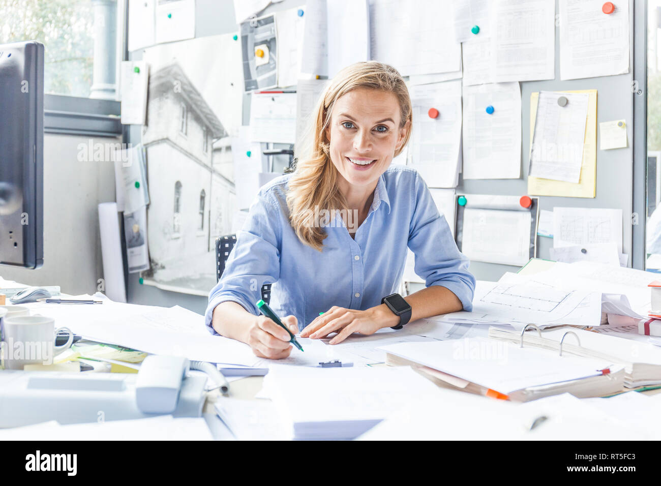 Portrait of smiling woman doing paperwork at desk in office Stock Photo