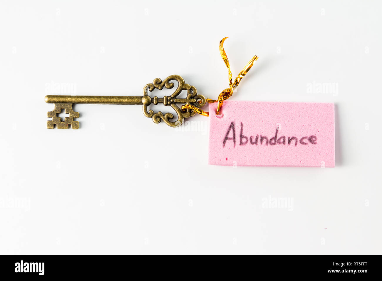 Close up of an ornamental key with the word abundance hand written on a pink tag isolated on a white background Stock Photo
