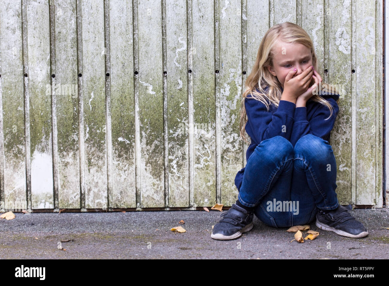 Frightened girl crouching in front of wooden wall Stock Photo