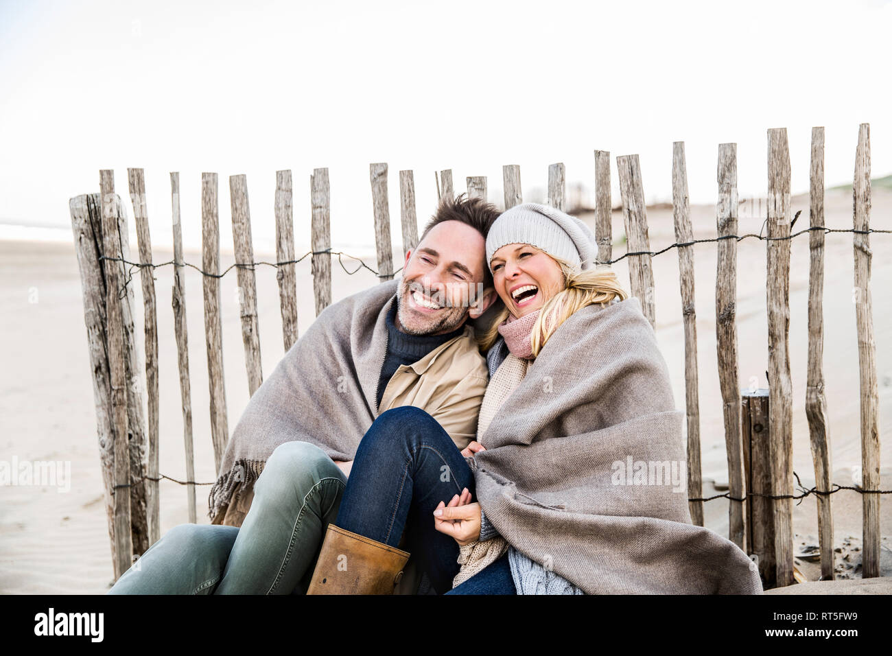 Happy couple wrapped in blanket on the beach Stock Photo