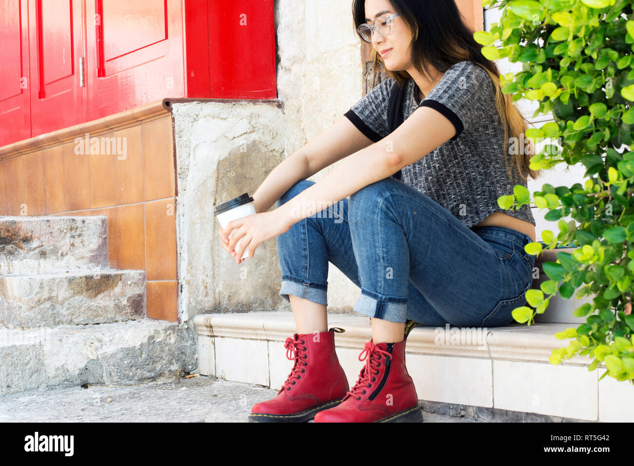 Fashionable young woman wearing  red boots sitting with coffee to go on steps Stock Photo
