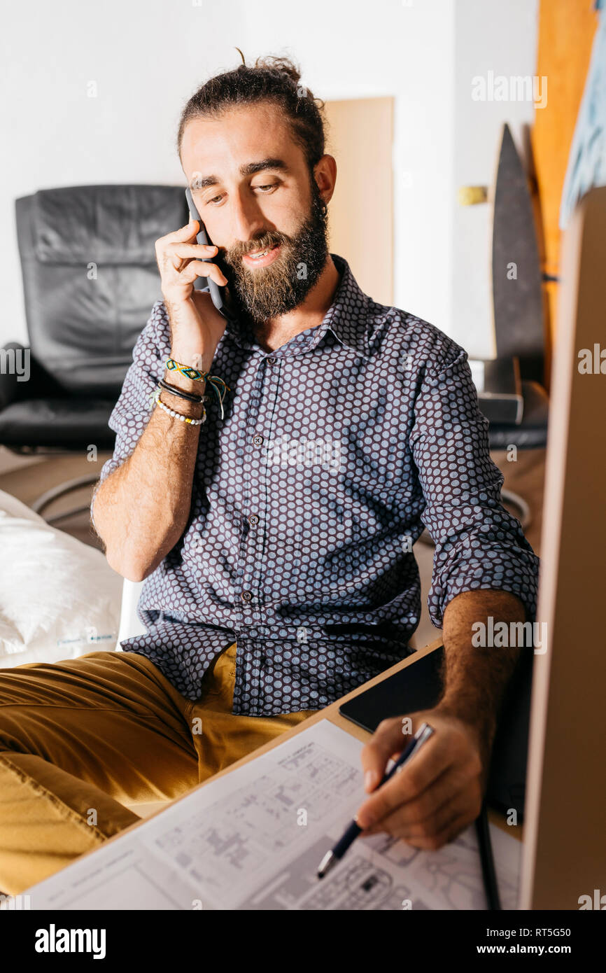 Young architect working at home with blueprints while talking on the phone Stock Photo