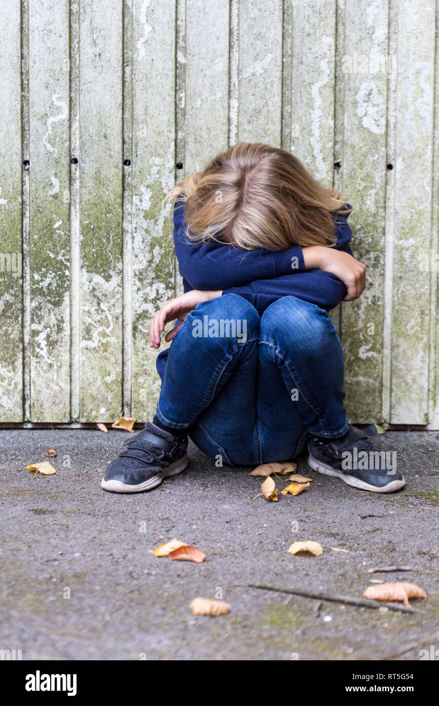 Sad girl crouching in front of wooden wall hiding her face Stock Photo