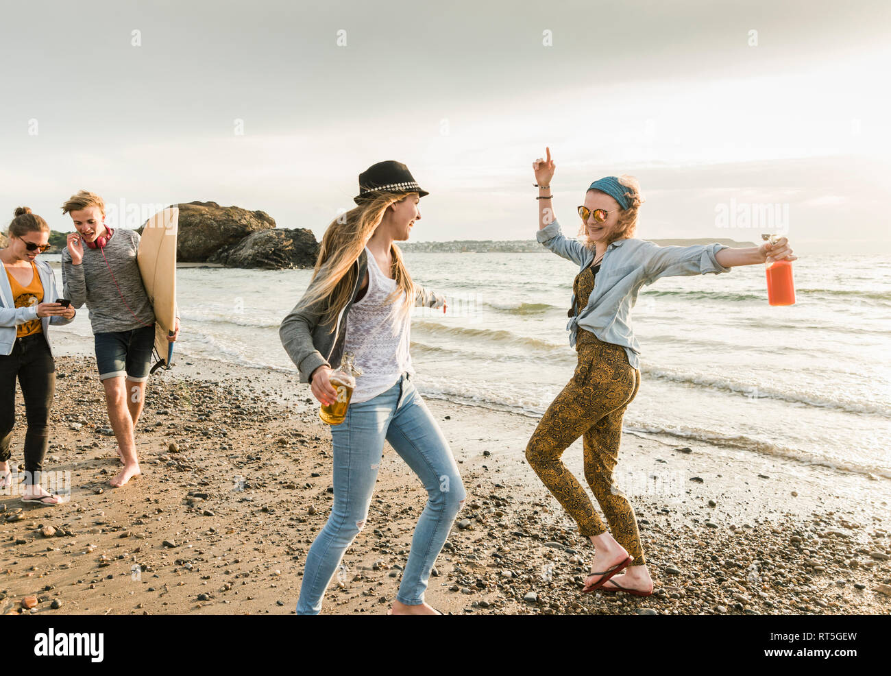 Happy friends with surfboard and drinks walking on stony beach Stock Photo