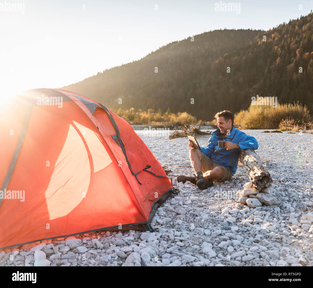Mature man camping at riverside, using tablet Stock Photo