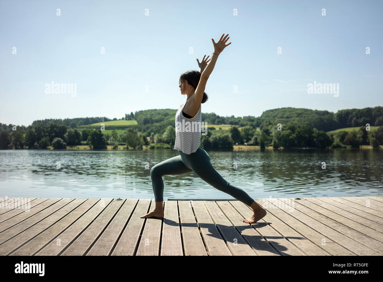 Mature woman practicing yoga in summer on a jetty at a lake Stock Photo