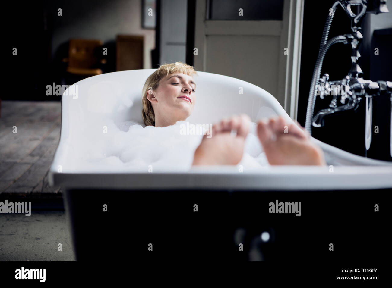 Blond woman taking bubble bath in a loft Stock Photo