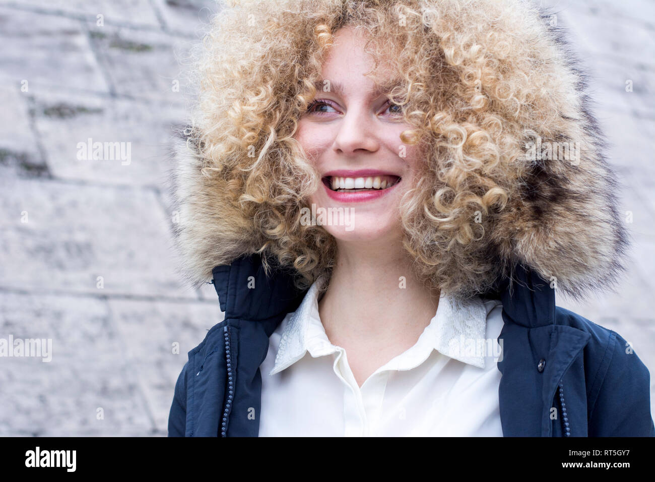 Portrait of laughing blond woman with ringlets wearing fur hood Stock Photo