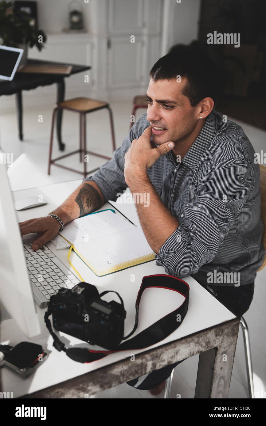 Young man with camera sitting at desk using computer Stock Photo