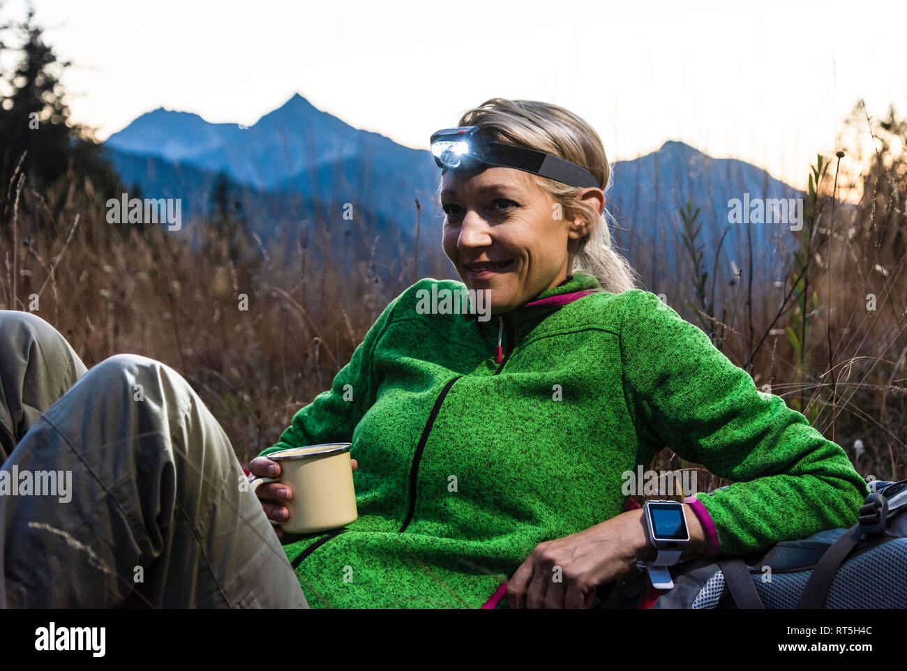 Hiking woman taking a break, drinking tea, wearing head lamp Stock Photo