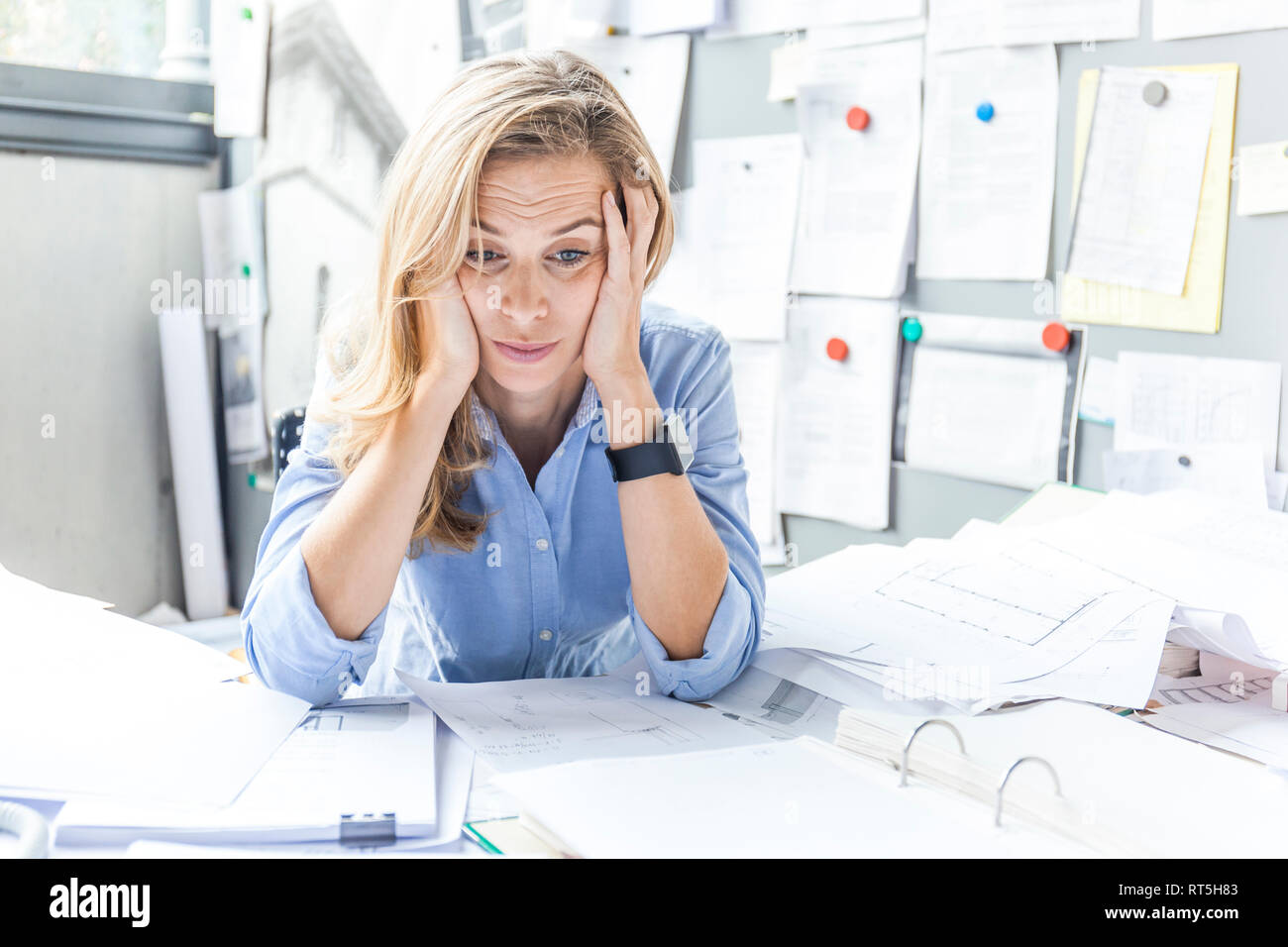 Stressed woman sitting at desk in office surrounded by paperwork Stock Photo
