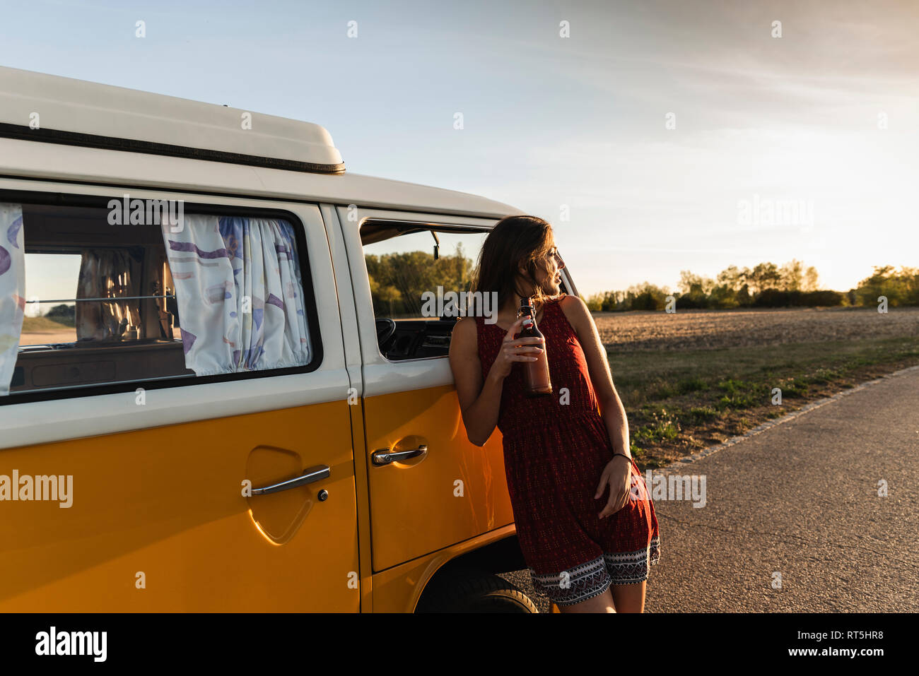 Pretty woman on a road trip with her camper, taking a break at sunset ...