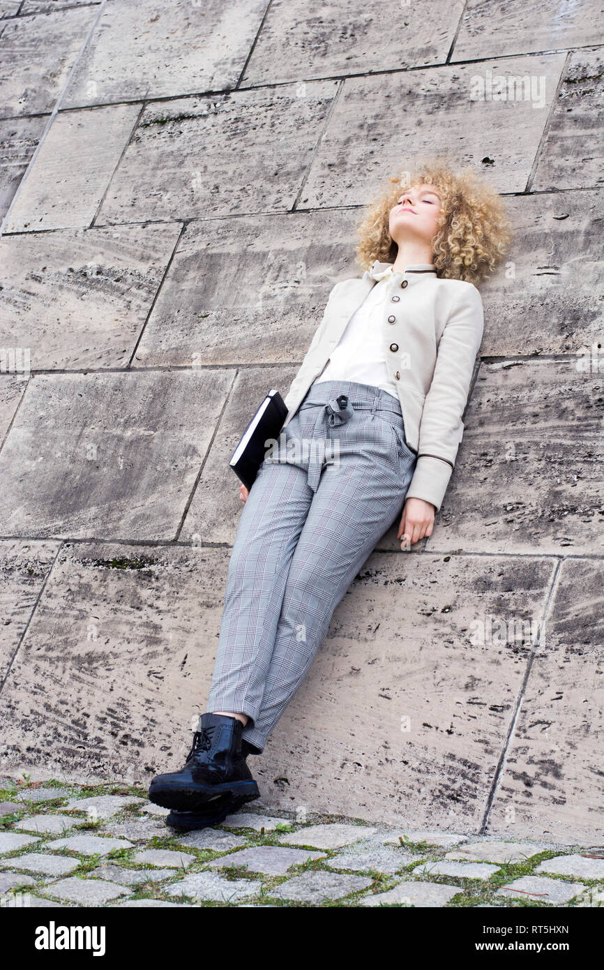 Fashionable blond woman with folder leaning against wall having a rest Stock Photo