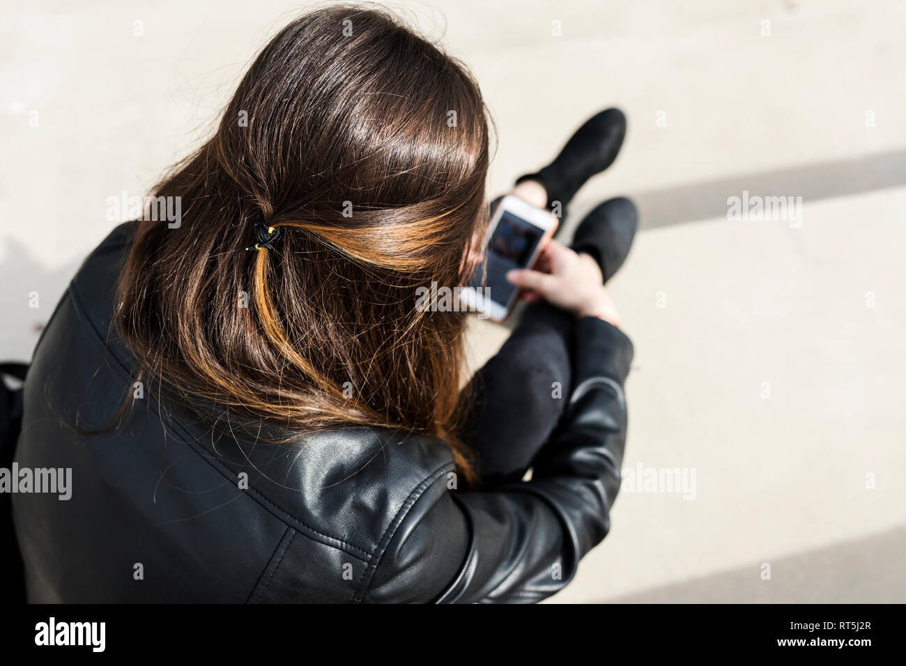 Rear view of young woman sitting outdoors using cell phone Stock Photo