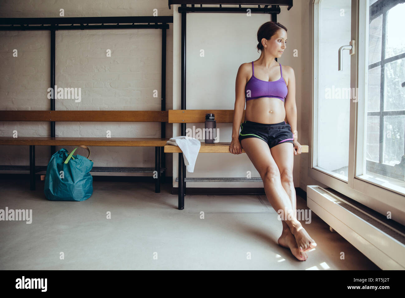 Sporty pregnant woman sitting in locker room looking out of window Stock Photo