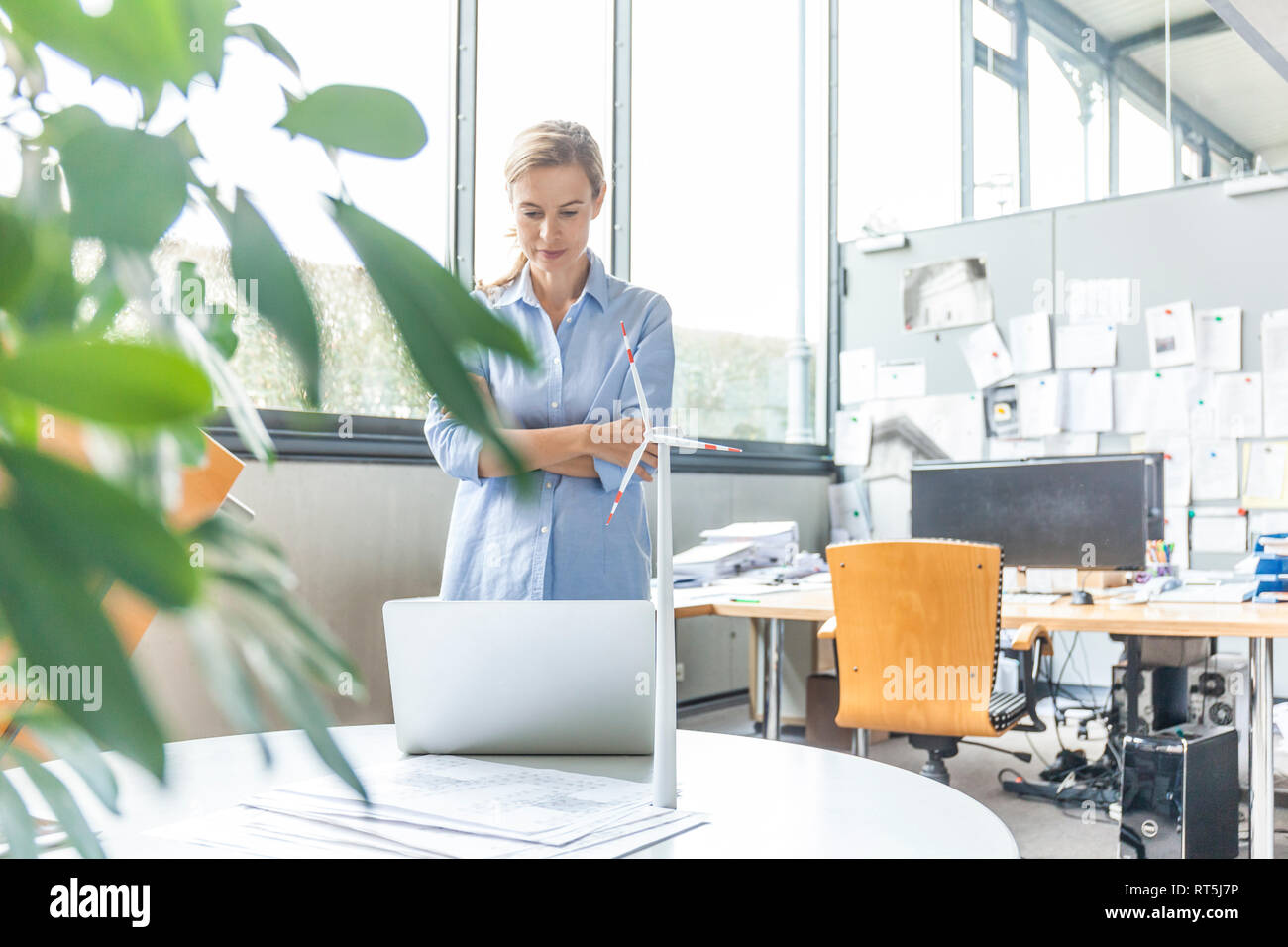 Woman in office with plan, laptop and wind turbine model on table Stock Photo