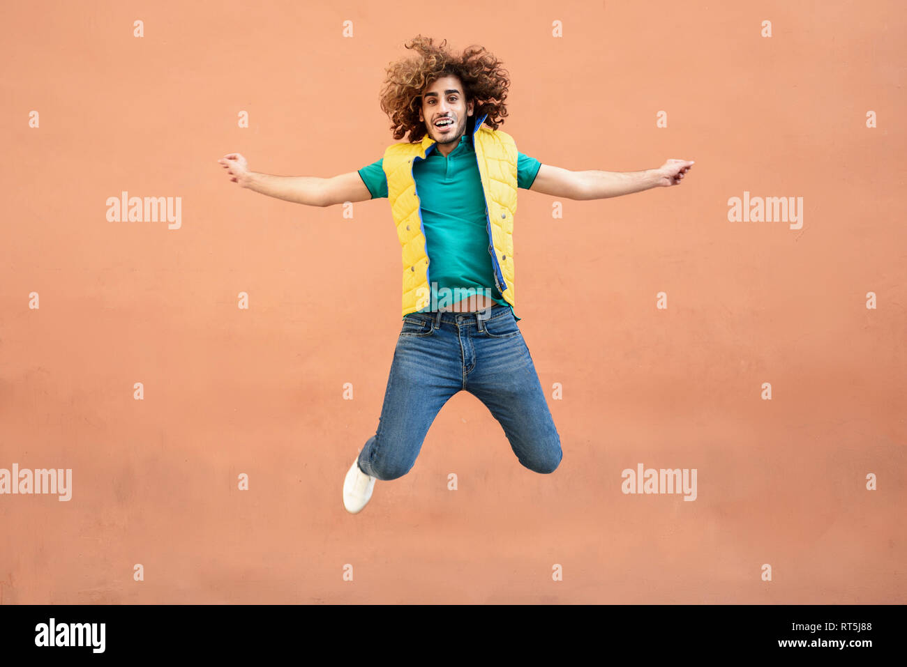 Portrait of smiling young man with curly hair wearing yellow waistcoat jumping in the air Stock Photo