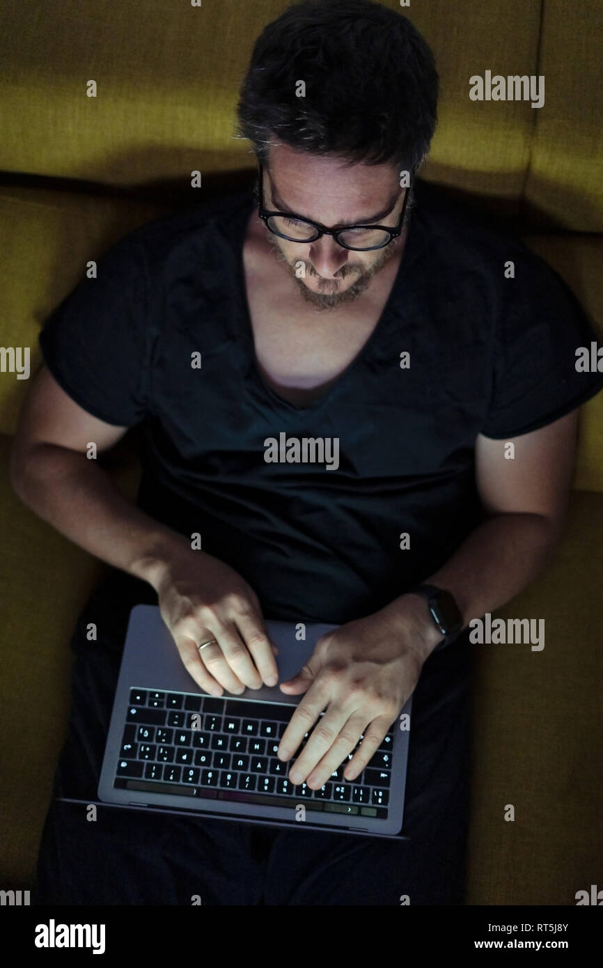 Man sitting on couch using laptop at night Stock Photo