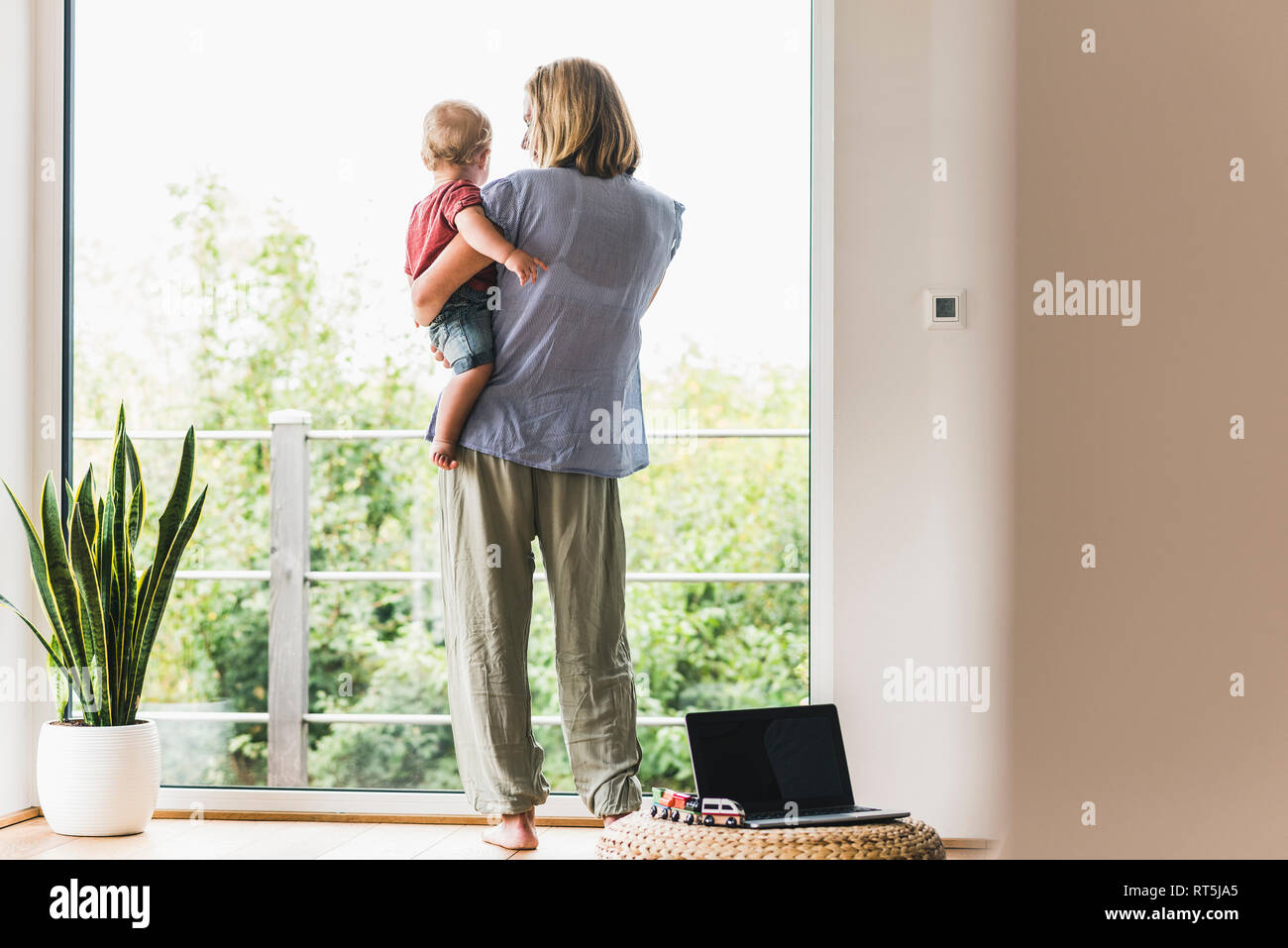 Mother carrying son, looking out of window Stock Photo