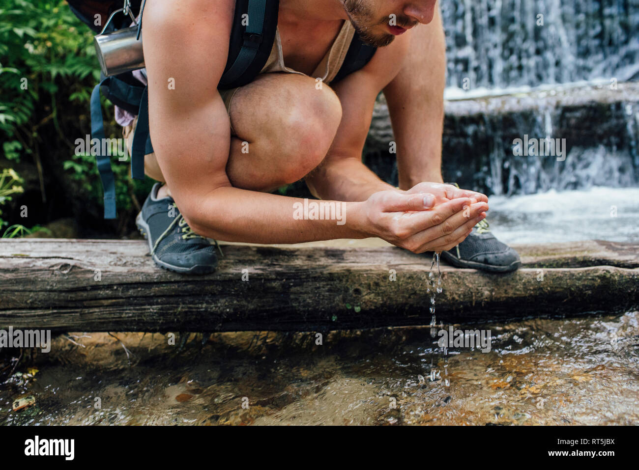 Young hiker with backpack refreshing at water in a forest, partial view Stock Photo