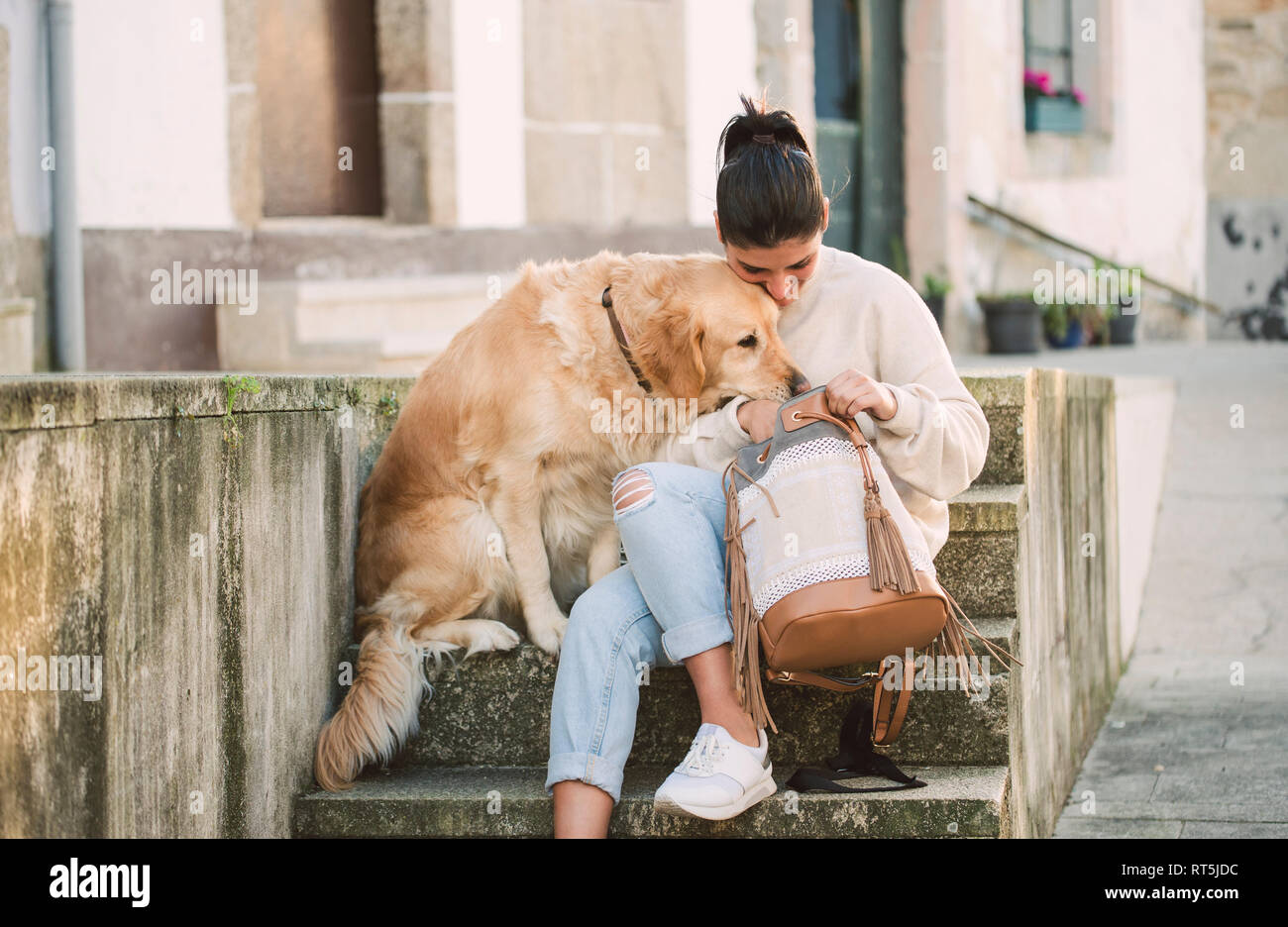 Young woman with her Golden retriever dog on stairs looking in backpack Stock Photo