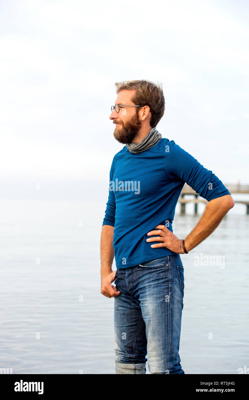Germany, Rerik, bearded man in front of the sea looking at distance on hazy day Stock Photo