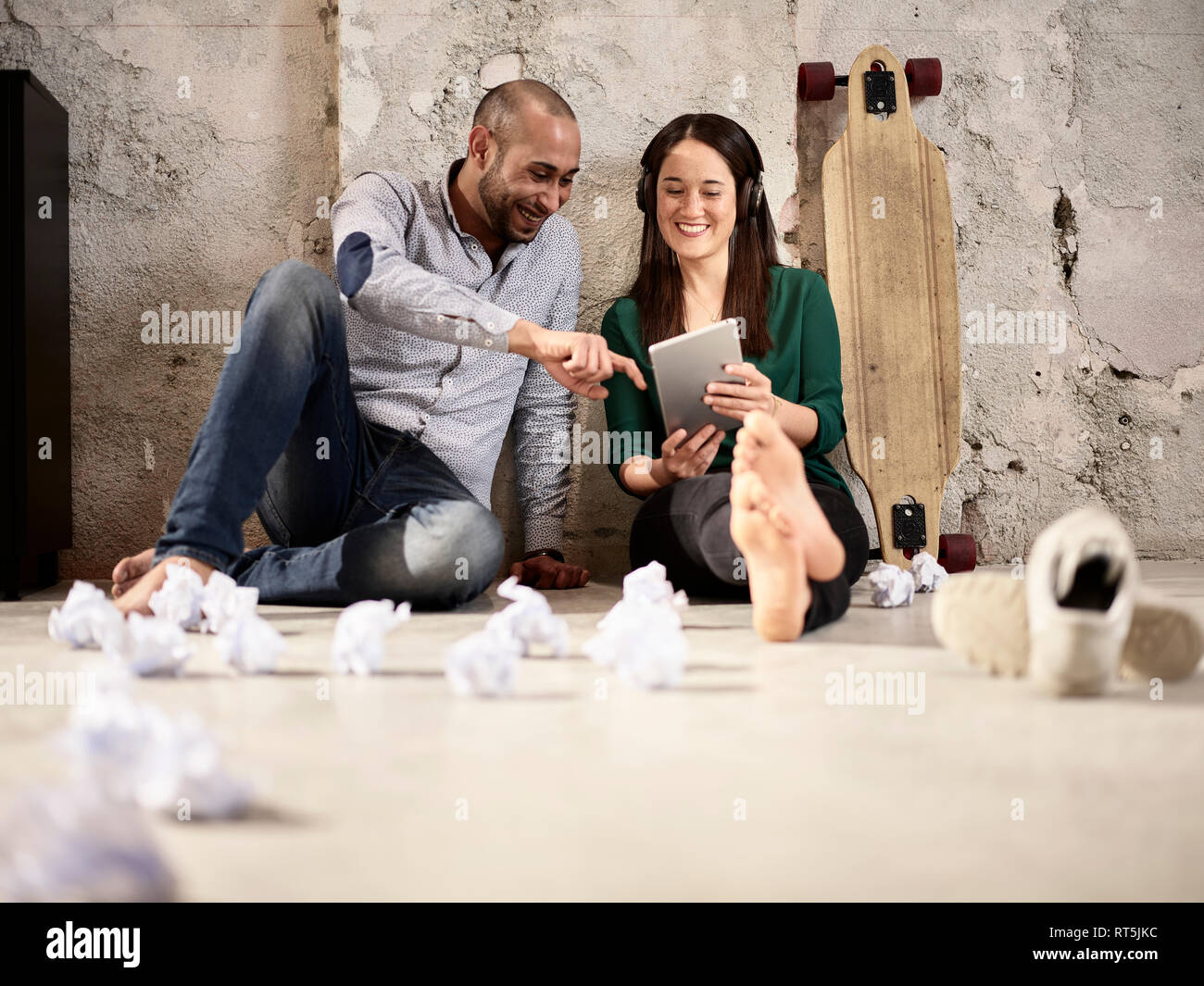 Smiling colleagues sitting on office floor sharing tablet Stock Photo