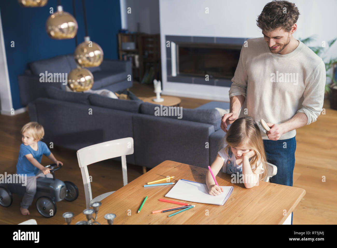 Father brushing daughter's hair, while she is drawing Stock Photo