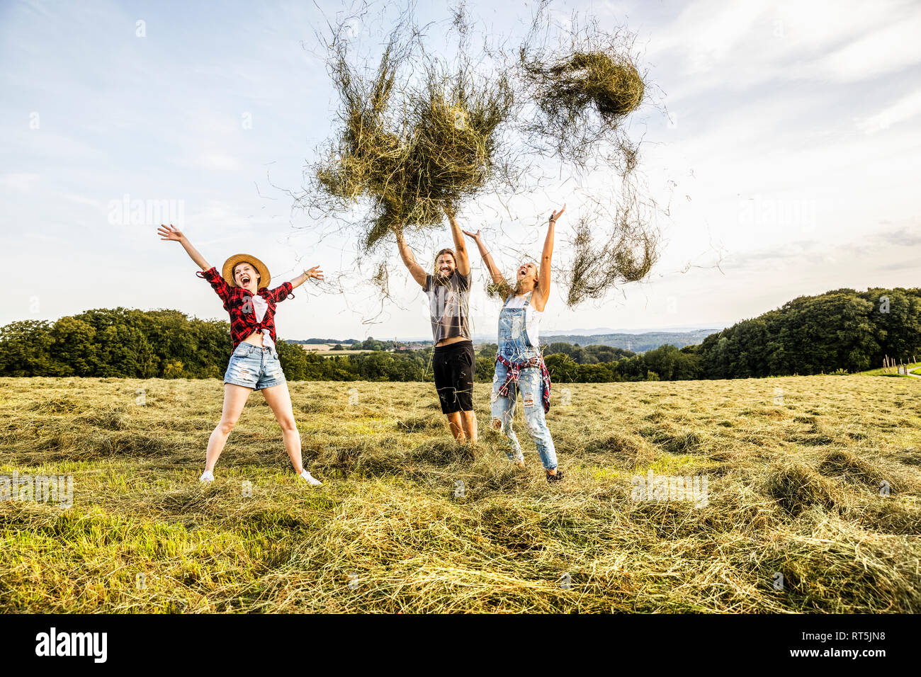 Carefree friends throwing hay in a field Stock Photo