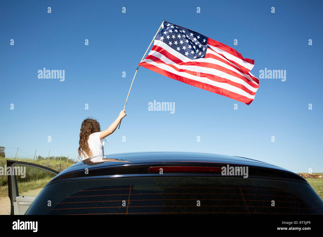 Girl holding American flag out of a car under blue sky Stock Photo - Alamy