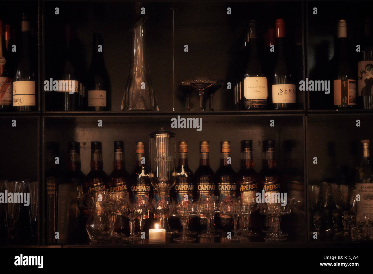 Several cocktail glasses and bottles of wine, Campari and Aperol on the shelves behind a bar. Stock Photo