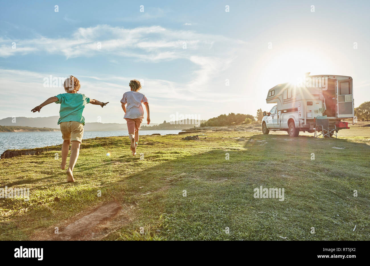 Chile, Talca, Rio Maule, two boys running on meadow beside camper at lake Stock Photo
