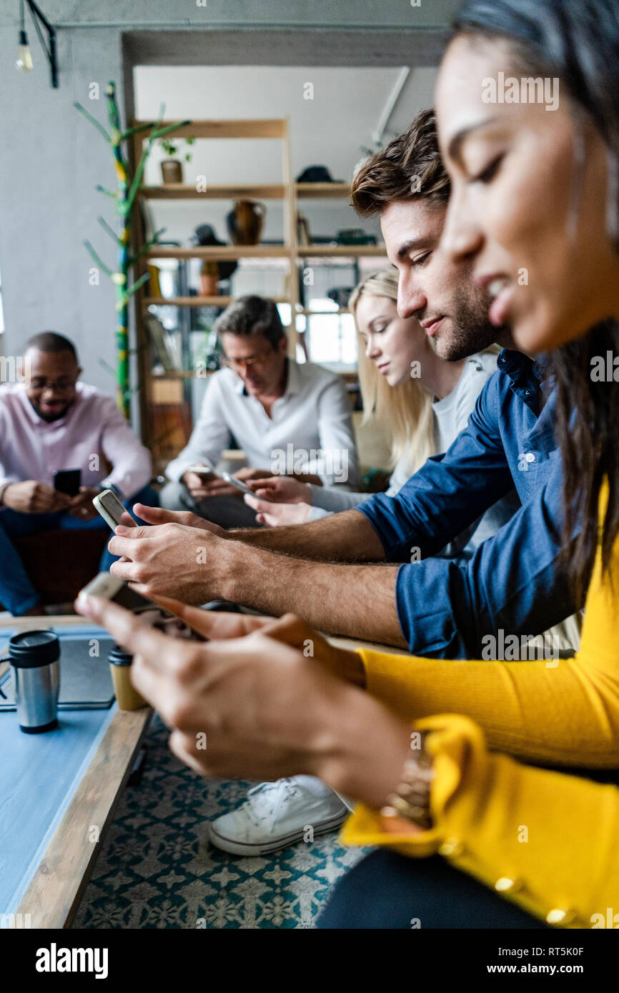 Business team sitting in loft office using cell phones Stock Photo - Alamy