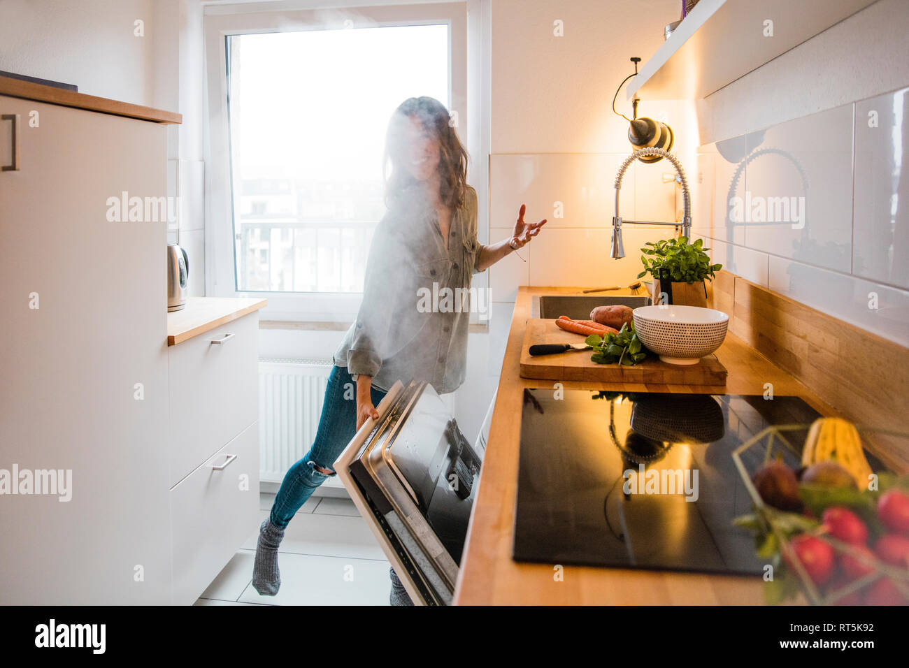Woman opening steaming dish washer in the kitchen Stock Photo