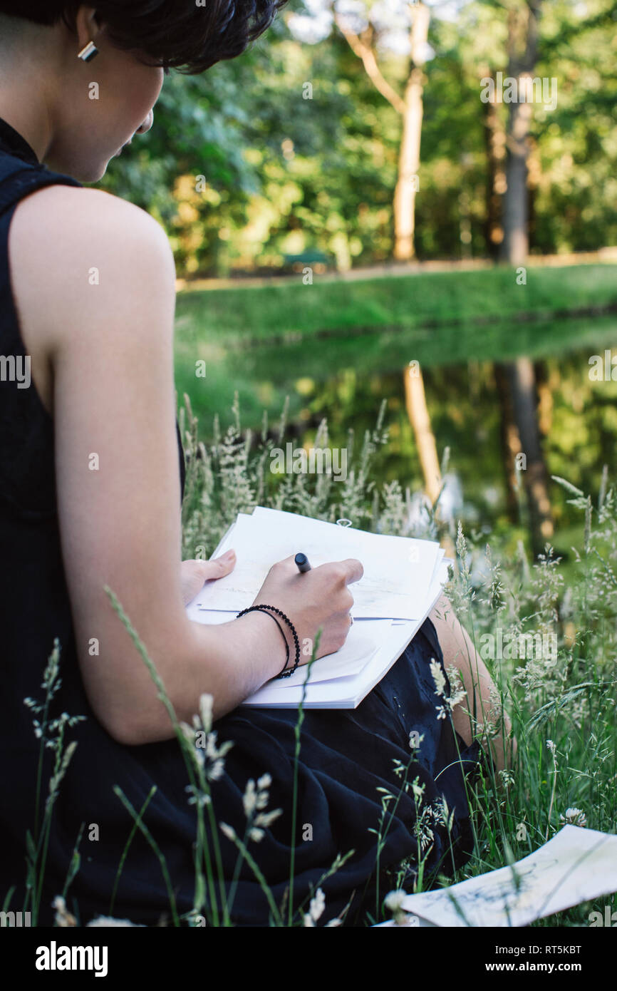 Artist sitting on a meadow near water drawing, partial view Stock Photo