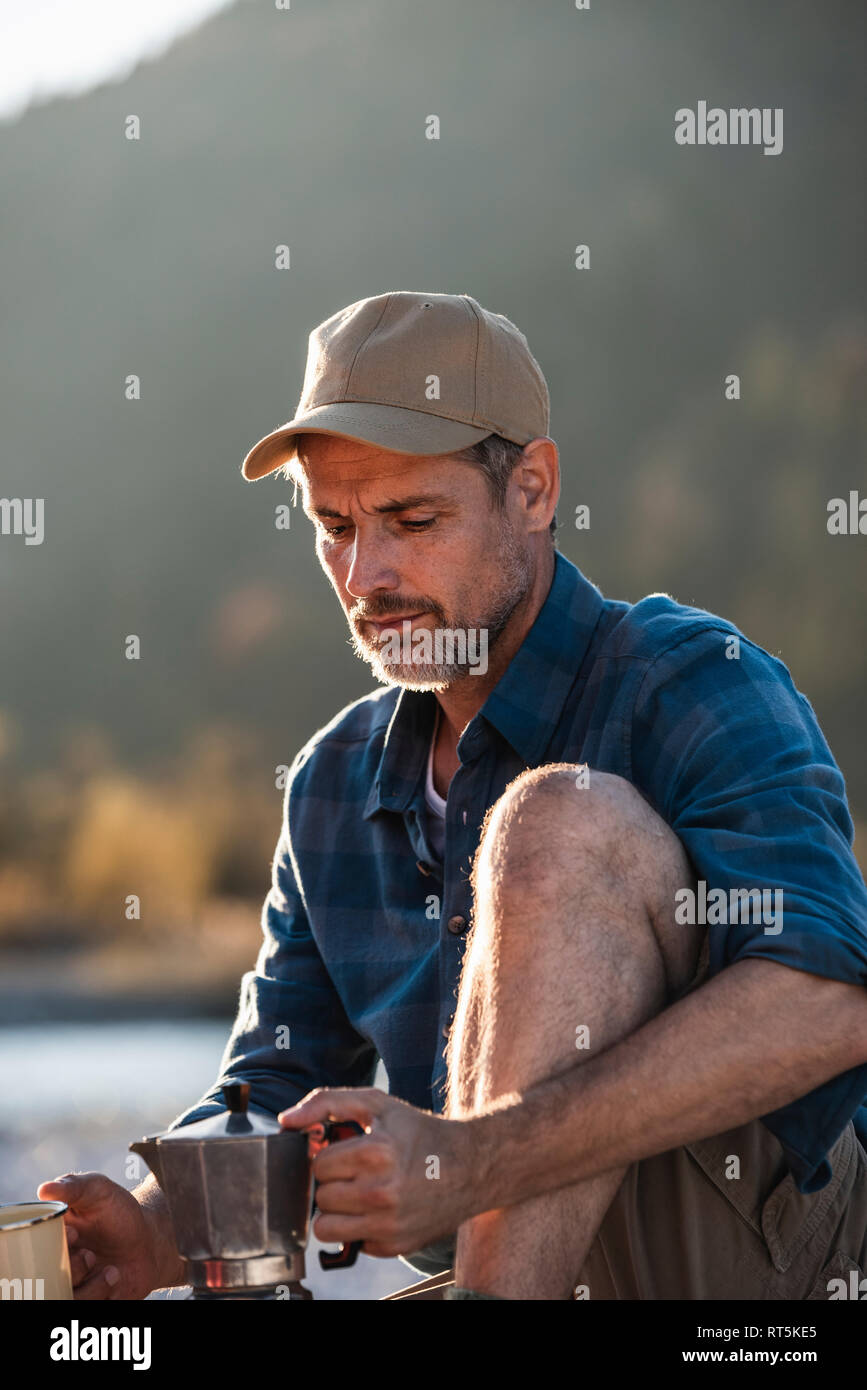 Mature man camping at riverside, using espresso machine Stock Photo