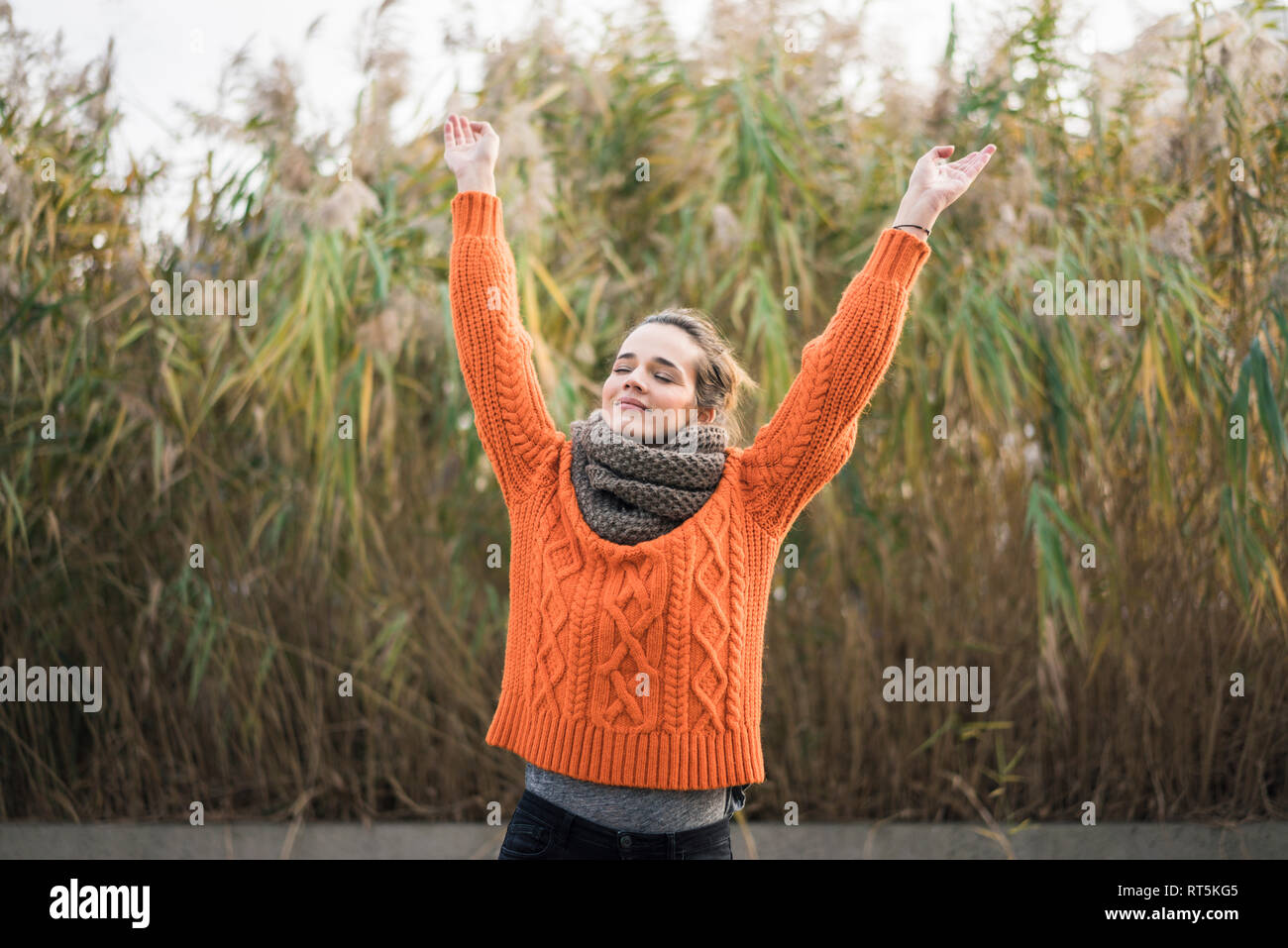 Portrait of smiling woman wearing orange knit pullover and scarf in autumn Stock Photo