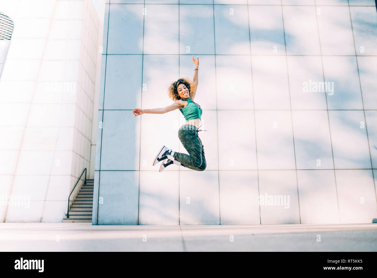 Portrait of happy young woman jumping at a building Stock Photo
