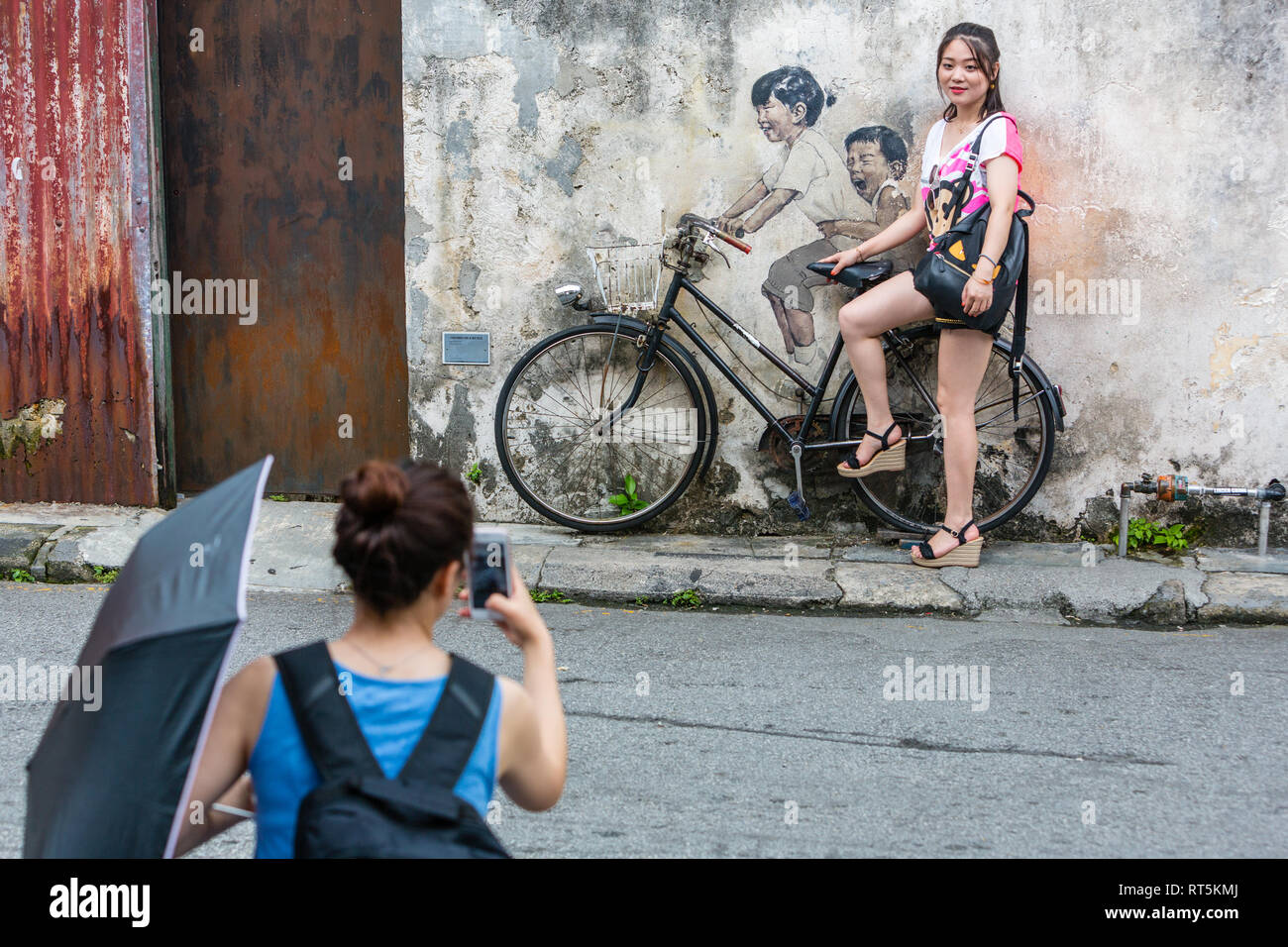 George Town, Penang, Malaysia.  Young Woman Posing for Photo by Street Art by Ernest Zacharevic. Stock Photo