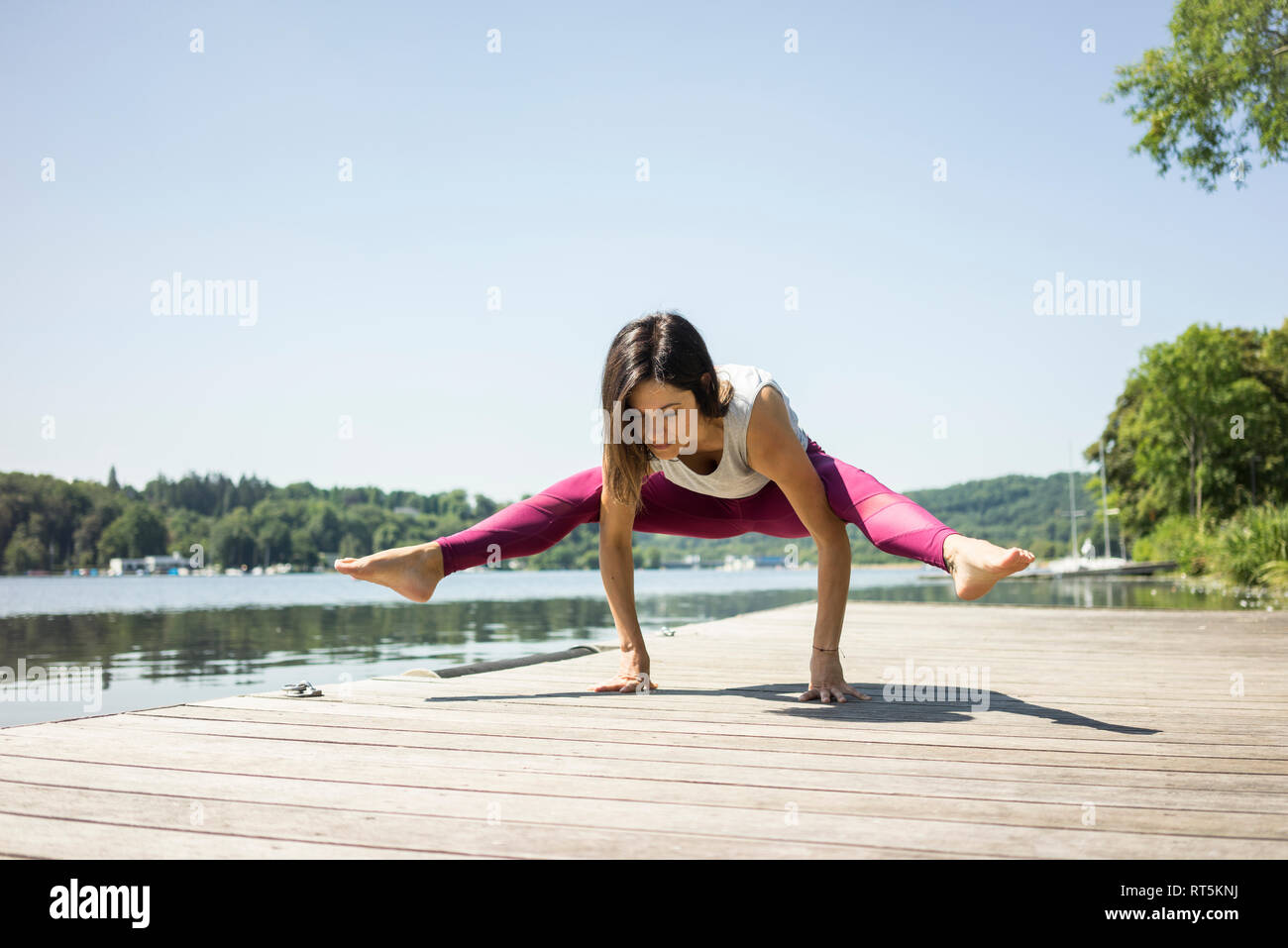 Mature woman practicing yoga in summer on a jetty at a lake Stock Photo