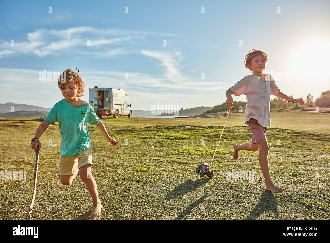 Chile, Talca, Rio Maule, two boys running on meadow with toy cars beside camper Stock Photo