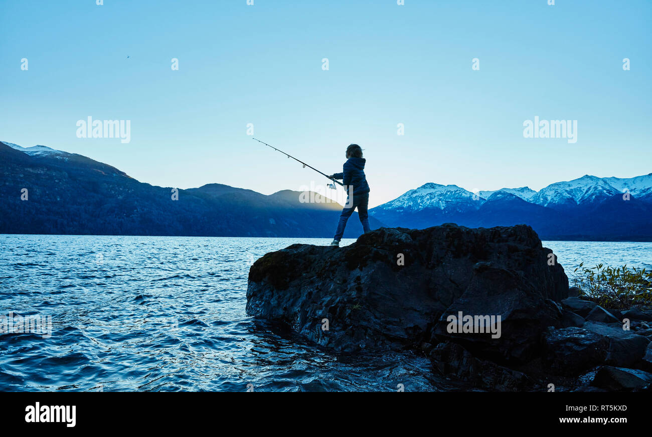 Argentina, Patagonia, Lago Futalaufquen, boy fishing in lake at dusk Stock Photo