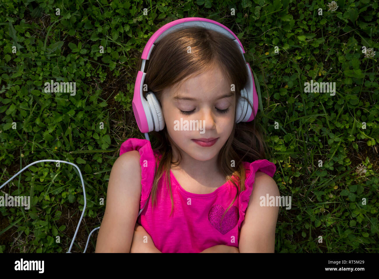Portrait of girl lying on a meadow listening music with pink headphones Stock Photo